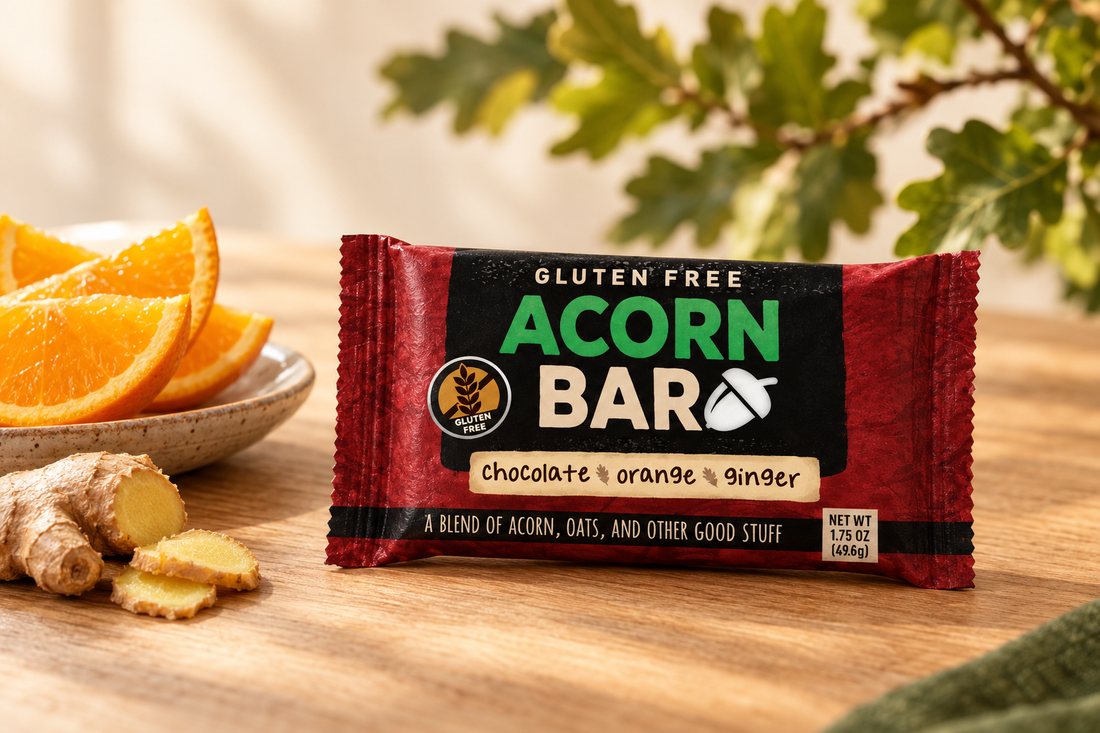  Acornbar.com Chocolate Orange Ginger snack bar on an oak tabletop with orange slices and ginger, against a softly blurred oak-leaf background. ⠋
