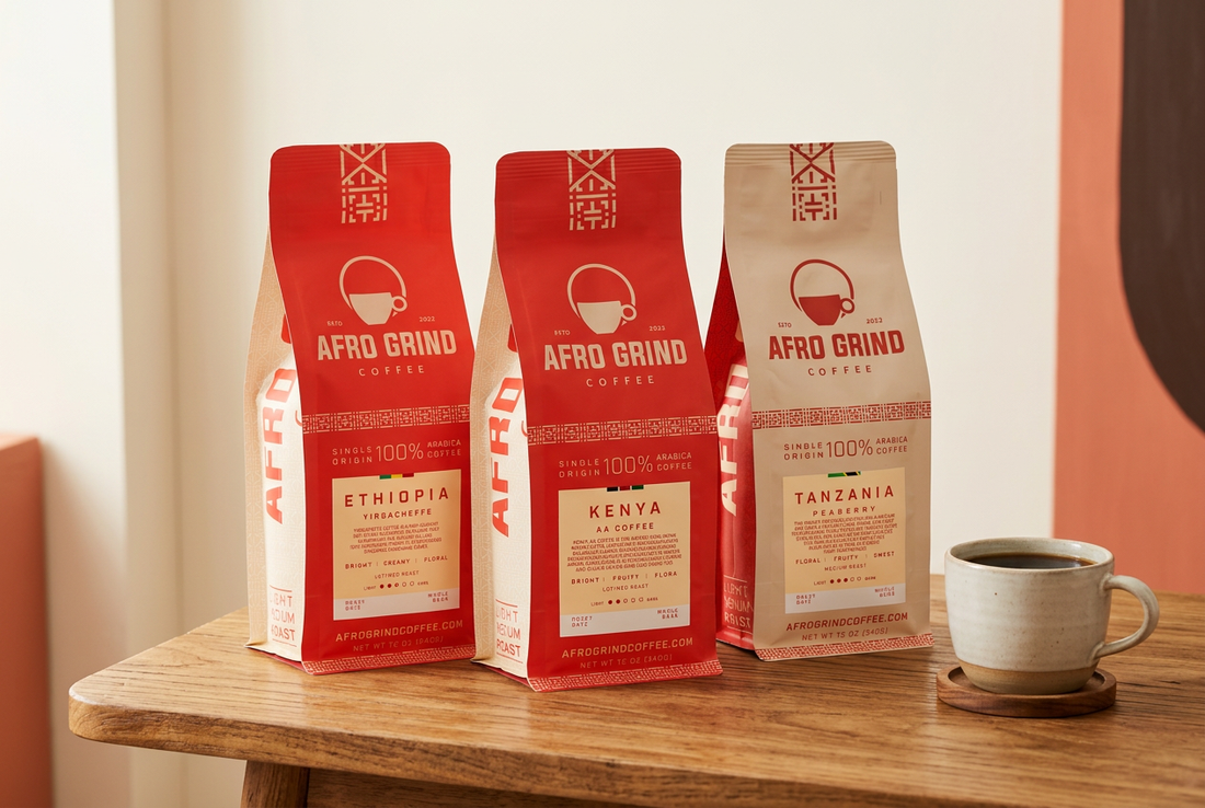 Afro Grind Coffee Ethiopia Yirgacheffe, Kenya AA, and Tanzania Peaberry bags beside a cup of black coffee on a wooden table.