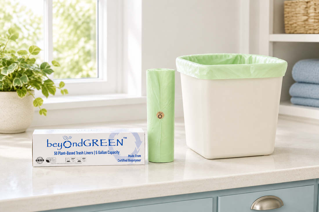 beyondGREEN plant-based trash liner carton and light-green roll beside a lined cream waste bin on a bright off-white countertop.