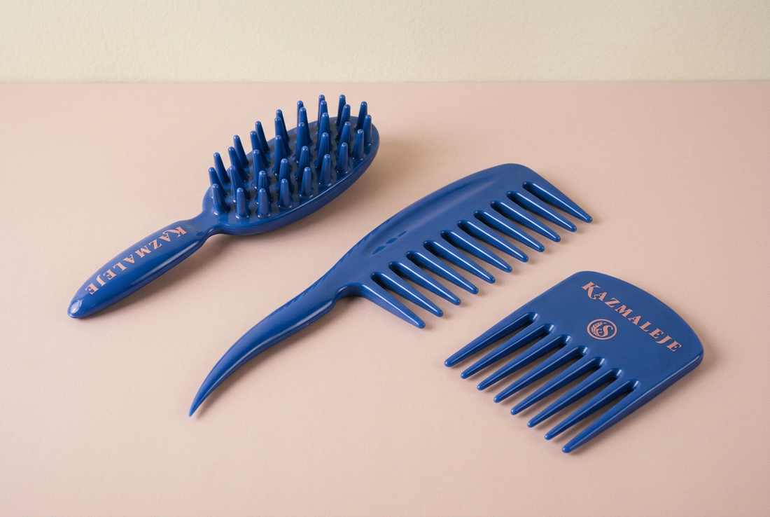 Blue KAZMALEJE KurlsPlus Paddle Comb, Comb, and Pick with rose lettering arranged on a pale rose surface.