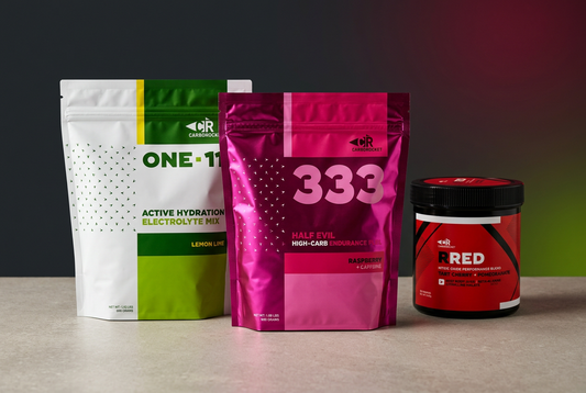 Carborocket ONE-11 hydration and magenta 333 endurance fuel pouches beside a red-and-black RRED jar on a pale stone surface against a charcoal background.