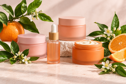 FIG Beauty & Skincare editorial still life of unlabelled pink and orange skincare containers with fresh leaves and citrus, representing plant-based beauty.