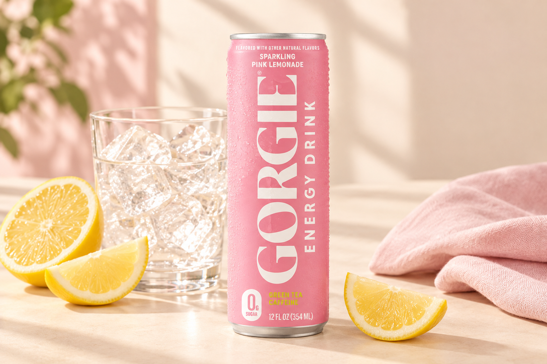 GORGIE Sparkling Pink Lemonade energy drink can beside a glass of ice, lemon slices, and pale-pink linen on a cream tabletop.