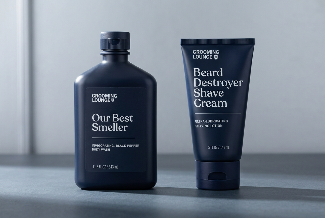 Grooming Lounge Our Best Smeller body wash beside a Beard Destroyer Shave Cream tube on a slate counter with silver-grey surroundings.