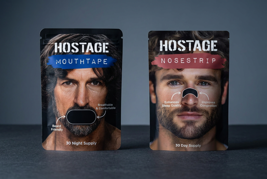 Hostage Mouth Tape and Hostage Nose Strip pouches with blue and muted red label bands on a charcoal surface.