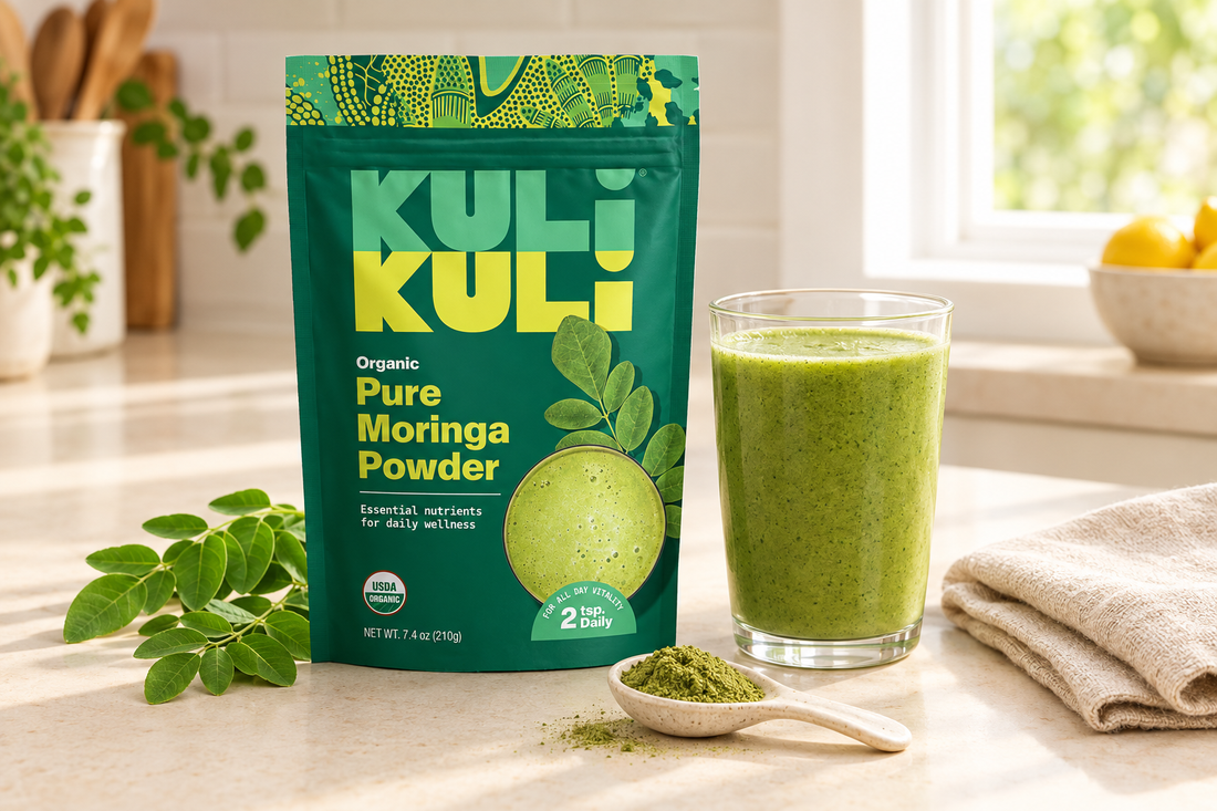 Kuli Kuli Foods Organic Pure Moringa Powder pouch beside a green smoothie, a spoon of green powder, and natural linen on a cream countertop.