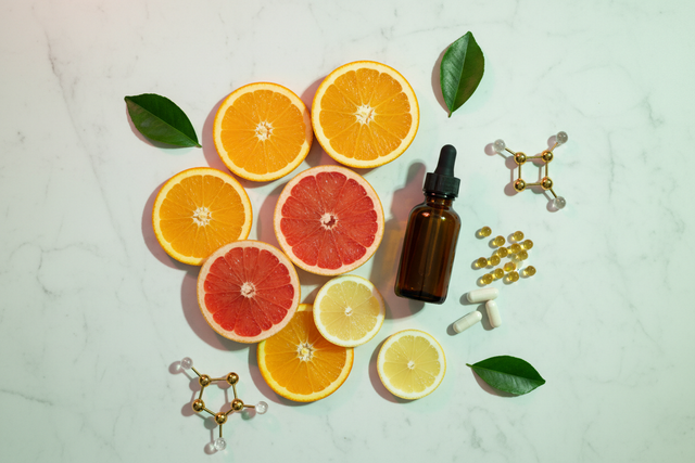 Fresh sliced oranges, a dark supplement bottle, and liposomal capsules on white marble — liposomal vs. regular vitamin C absorption science