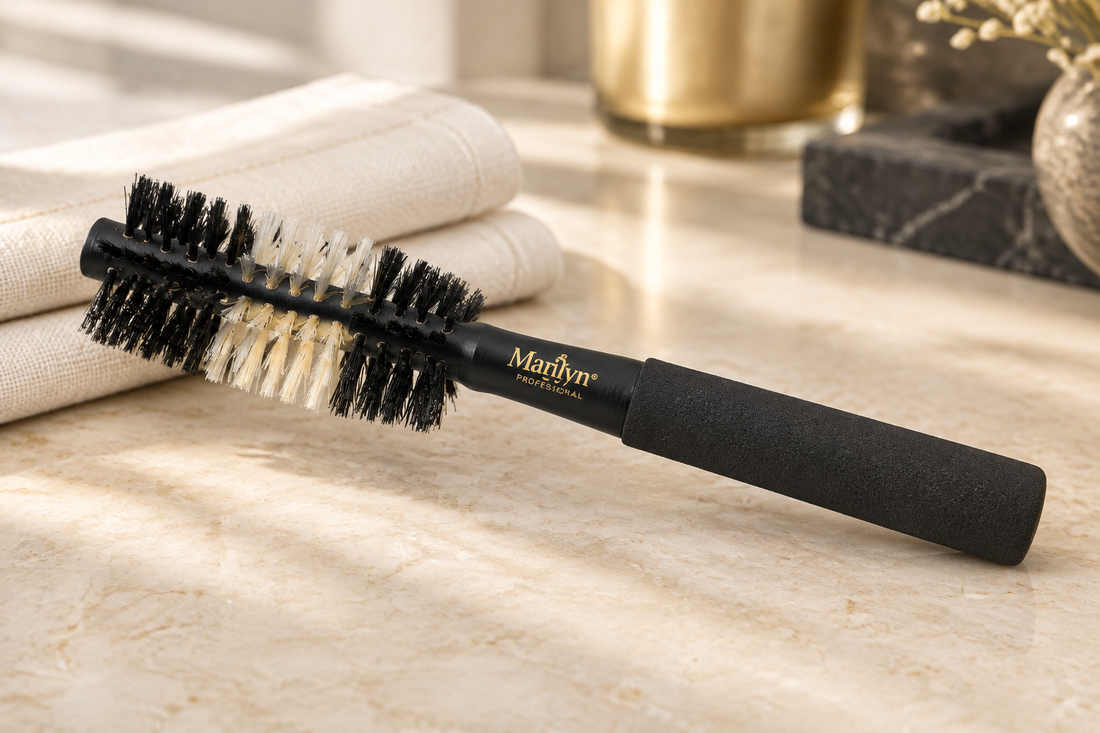 Marilyn Brush Tuxedo Pro black hourglass round brush with contrasting bristles beside ivory linen on a cream stone vanity surface.