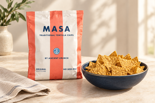 MASA Original tortilla chips bag beside a navy bowl of golden tortilla chips on a cream tabletop with a linen napkin.