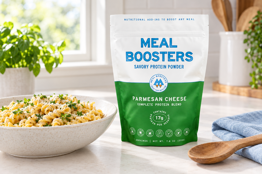 Meal Boosters Parmesan Cheese savory protein powder pouch beside a bowl of pasta, a wooden spoon, and pale-blue linen on a bright kitchen counter.