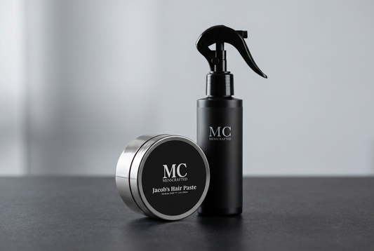 Menscrafted Jacob’s Hair Paste jar beside a black Sea Salt Spray bottle on a charcoal counter with soft silver-grey surroundings.
