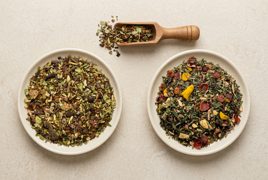 Two loose MoonMaid Botanicals herbal tea blends with dried leaves and spice pieces in cream dishes beside a wooden scoop.