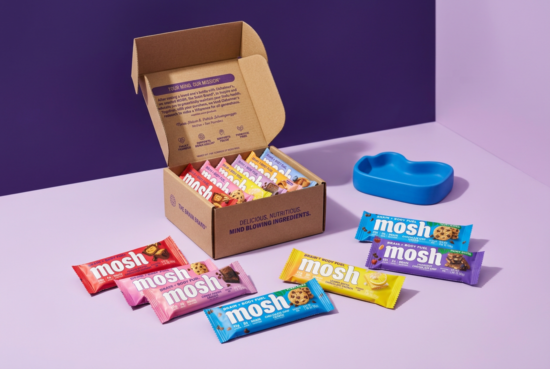 MOSH protein bars in colorful wrappers arranged beside an open kraft variety box on a pale lilac surface against a purple background.