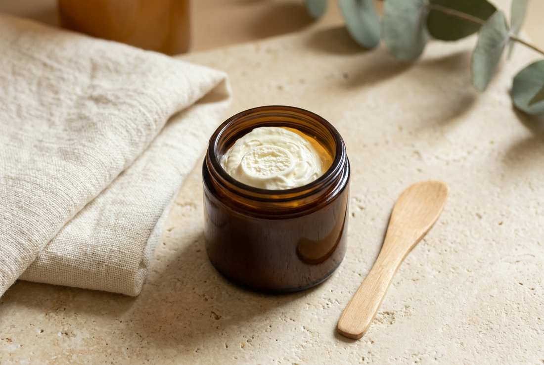 Open amber jar of Tallow Skin Co. Farm Silk whipped cream beside ivory linen and a wooden cosmetic spatula on a cream stone surface.