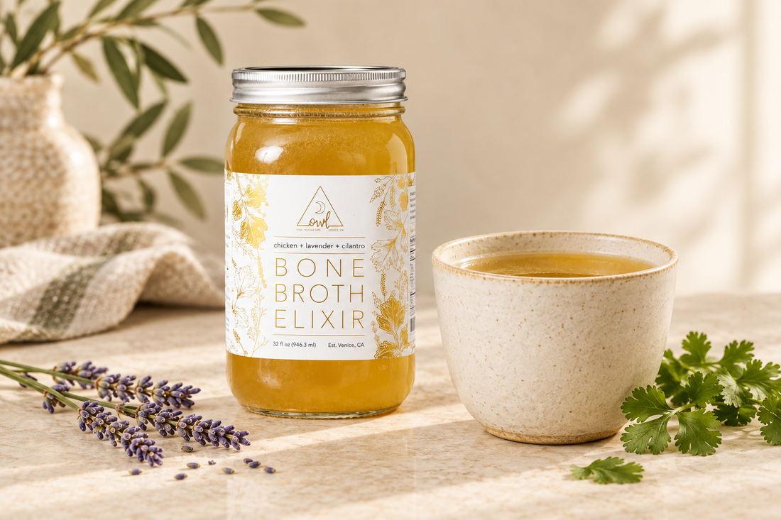 OWL Venice Chicken Bone Broth Elixir jar beside a ceramic cup of golden broth, lavender sprigs, and cilantro on a cream countertop.