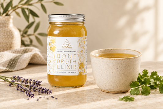 OWL Venice Chicken Bone Broth Elixir jar beside a ceramic cup of golden broth, lavender sprigs, and cilantro on a cream countertop.