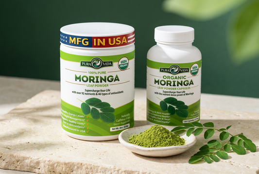 Pura Vida Moringa leaf powder tub and capsule bottle beside a small dish of green powder and moringa leaves on a cream surface against a forest-green background.