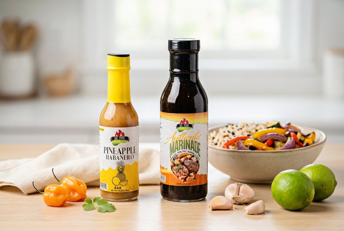 Su Yum Foods Pineapple Habanero Hot Sauce and Authentic Marinade bottles on a wooden table beside a bowl of rice and roasted vegetables.