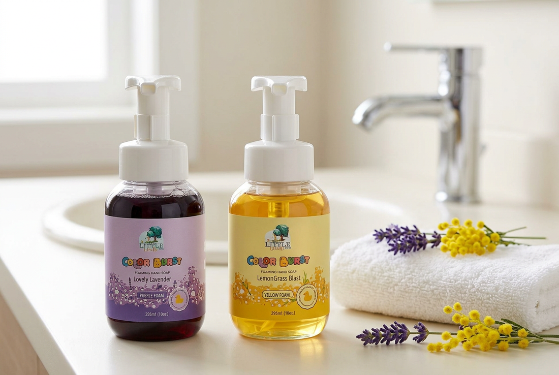 The Little Giraffe Color Burst Lovely Lavender and LemonGrass Blast foaming hand soap bottles on an ivory bathroom counter beside a folded white towel.