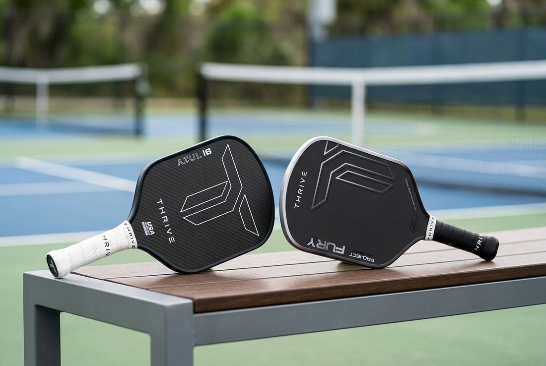 Thrive Pickleball AZUL paddle with a white grip and FURY Hybrid paddle with a black grip resting on a courtside bench.