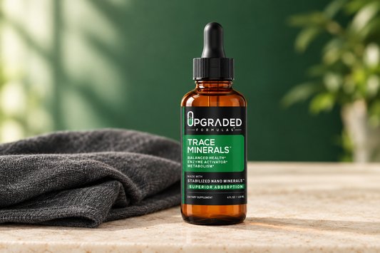 Upgraded Formulas Trace Minerals amber dropper bottle beside charcoal linen on a cream stone surface with a soft emerald background.
