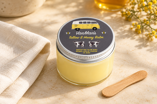 VanMan Tallow & Honey Balm jar with its yellow van lid design beside ivory linen and a wooden cosmetic spatula on a cream surface.