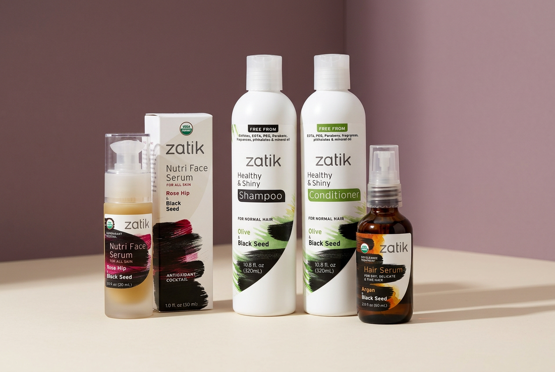 Zatik Naturals facial serum and botanical hair-care bottles arranged on an ivory surface against a soft plum background.