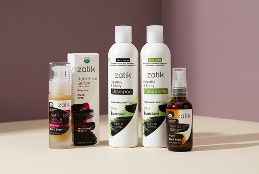 Zatik Naturals facial serum and botanical hair-care bottles arranged on an ivory surface against a soft plum background.