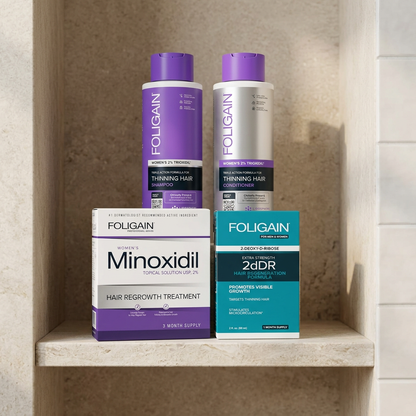FOLIGAIN women's minoxidil, 2dDR serum, shampoo and conditioner arranged on a neutral stone bathroom shelf.