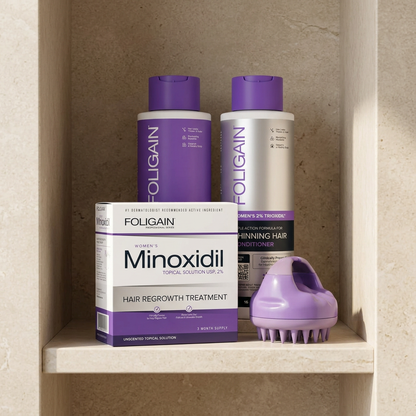 FOLIGAIN women's minoxidil, shampoo, conditioner and purple scalp massager arranged on a neutral stone bathroom shelf.