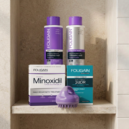 Women's FOLIGAIN minoxidil, 2dDR serum, shampoo, conditioner and purple massager arranged on a stone bathroom shelf.