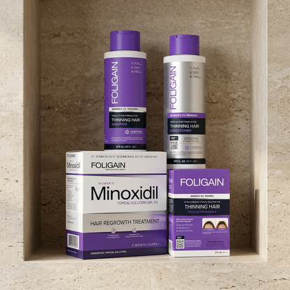 Women's FOLIGAIN complete hair care bundle with two treatment cartons in front of shampoo and conditioner on a stone bathroom shelf.