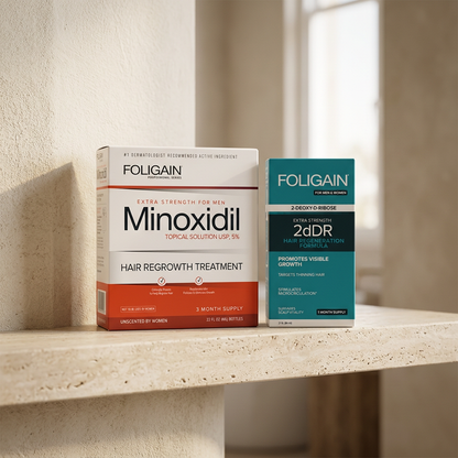 Boxed FOLIGAIN men's minoxidil and teal 2dDR serum duo on a warm neutral bathroom shelf.