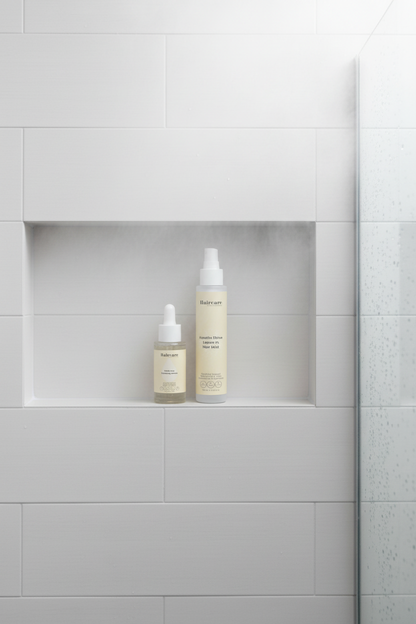 Scalp Care Exfoliating Serum and Keratin Shine Leave-In Hair Mist on a white tile shower niche shelf with steam and water droplets — exfoliate and shine bundle by Daily Health & Beauty